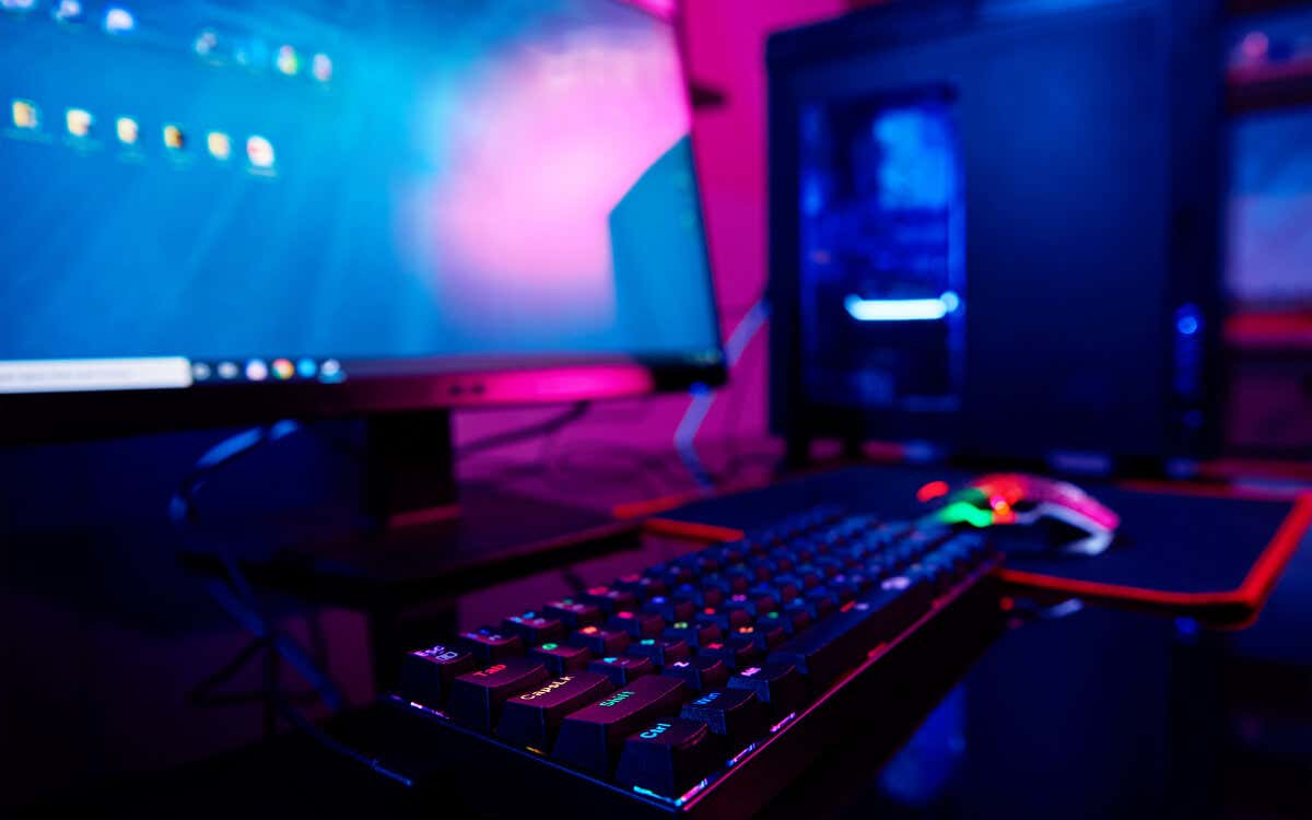 A computer setup, brightly lit in pink and blue hues, displays a game or program; a person is using a keyboard and mouse in a dimly lit room