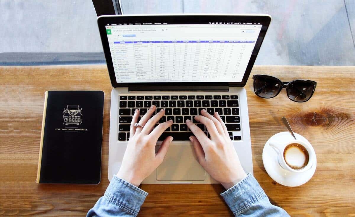 A laptop displays a spreadsheet; hands type on its keyboard